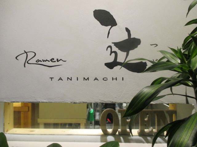 ラーメン 辻 の店舗外観。壁に「Ramen 辻 TANIMACHI」の筆文字看板と観葉植物、木製のOPENサイン